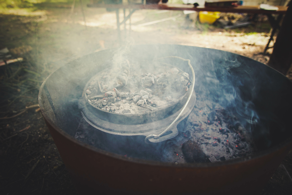 A Dutch Oven stands on hot, glowing coals in the smoke.